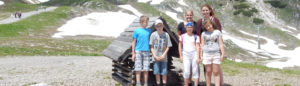 Freizeiten Kinder und Betreuer vor kleiner Holzhütte und Berglandschaft